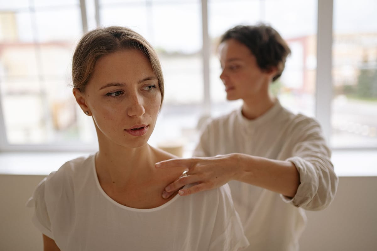 A clinician assessing a seated patient's neck and shoulder